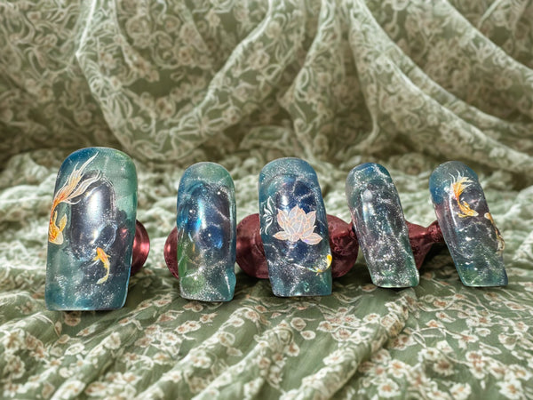 Set of five decorative nail art designs on a floral fabric background