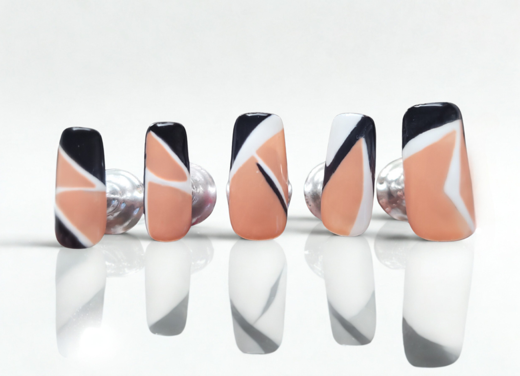 Set of nails with black, white, and peach design on a white background