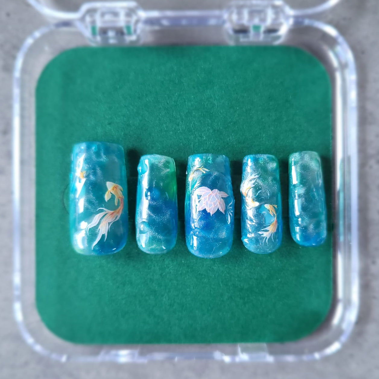 Set of blue nail art designs in a clear case on a green mat