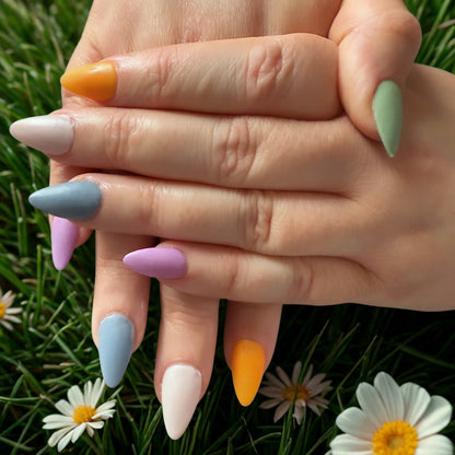 Close-up of hands with colorful nail polish on a grassy background with flowers.