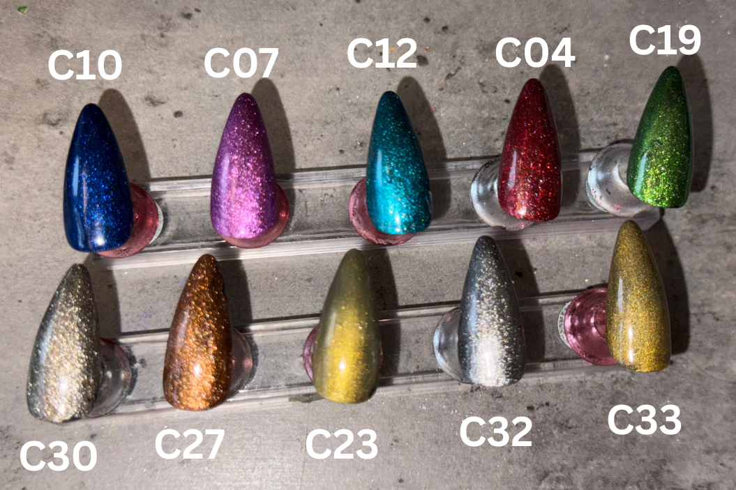Row of multicolored glittery nail tips with color labels on a concrete surface