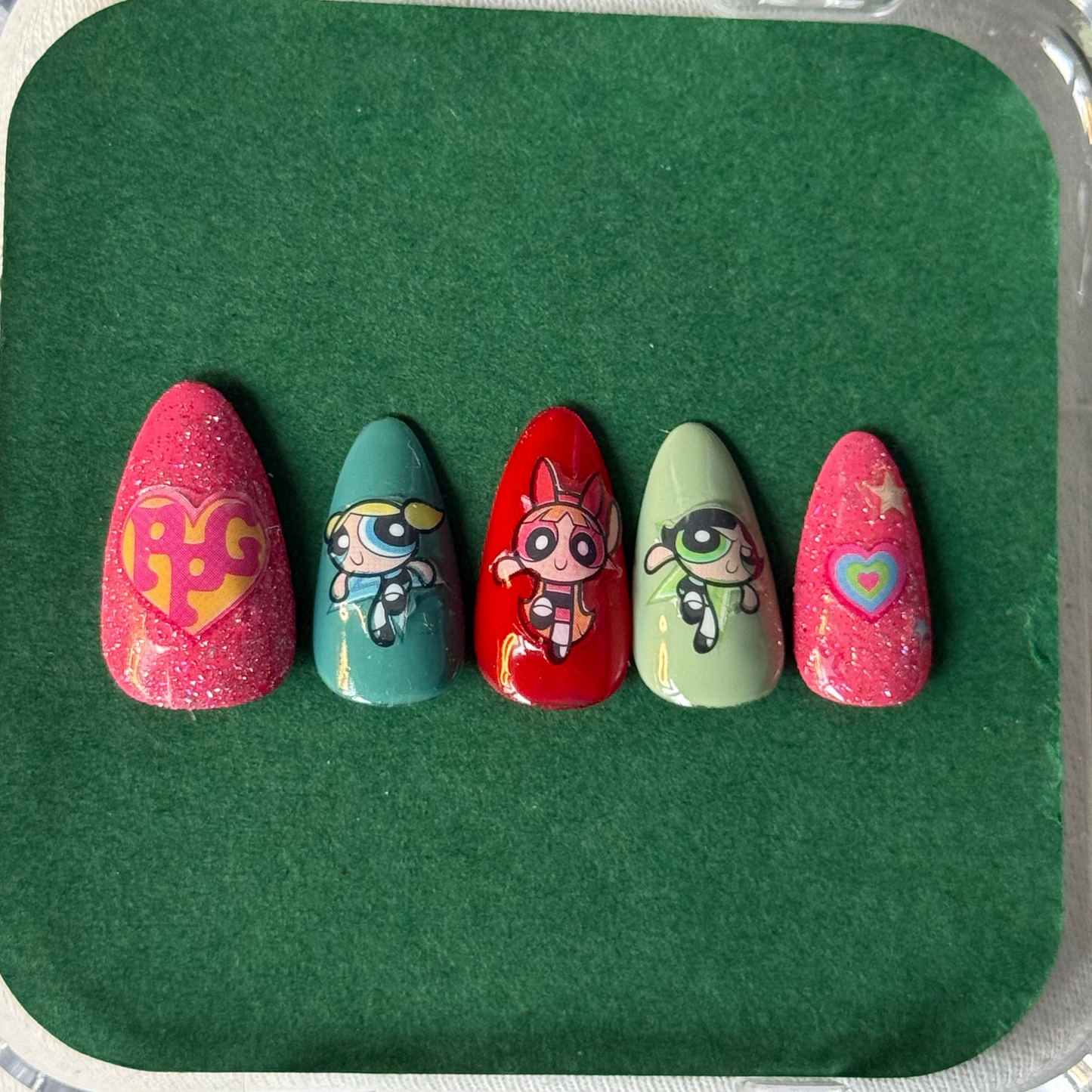Set of five painted nails with cartoon character designs on a green tray.