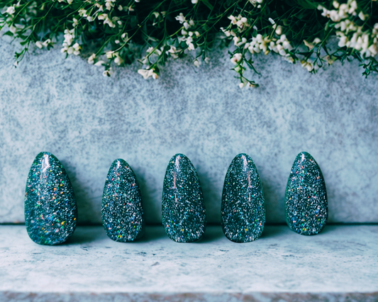 Five green glittery almond nails on a stone surface with a floral background