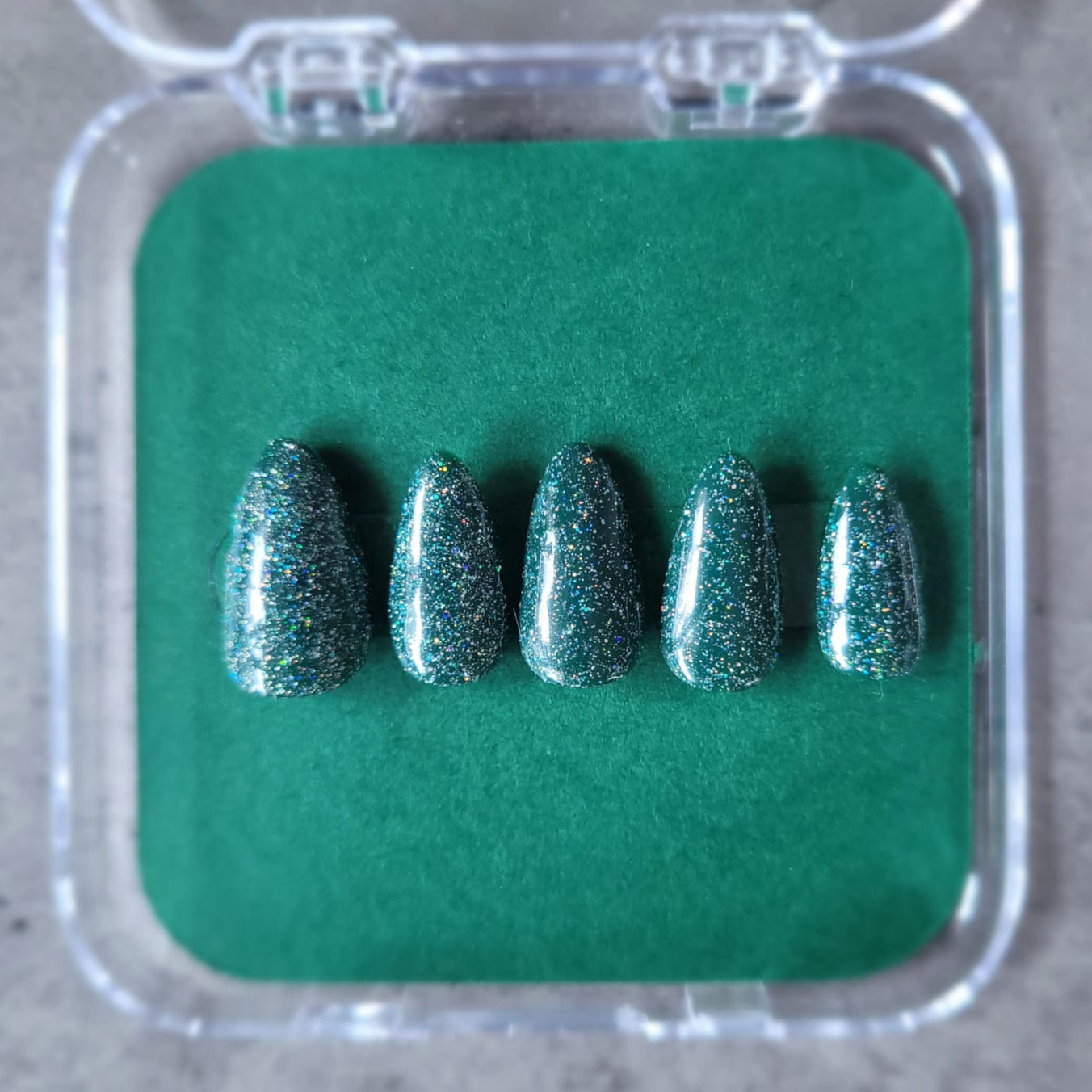 Five green glittery false nails in a clear case on a green background
